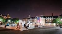 picture of market square with people sitting around a fountain and city hall lit up at night
